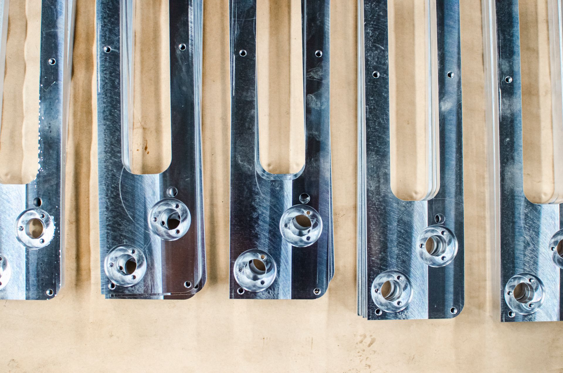 Metal brackets with rounded ends, drilled holes, and slots, lying on a light brown surface.