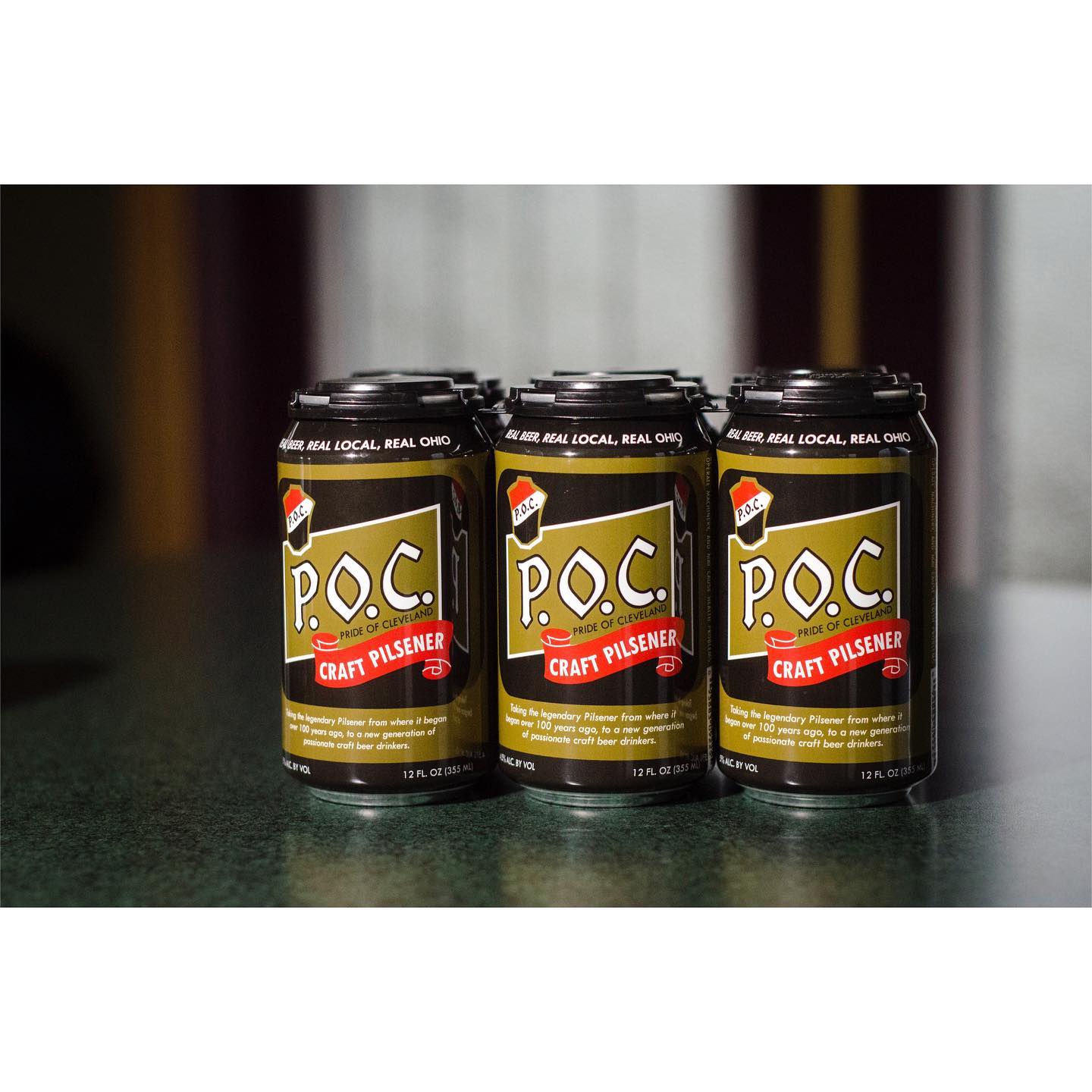 Three cans of P.O.C. Crazy Possum soda, brown and gold label, on a dark green surface.