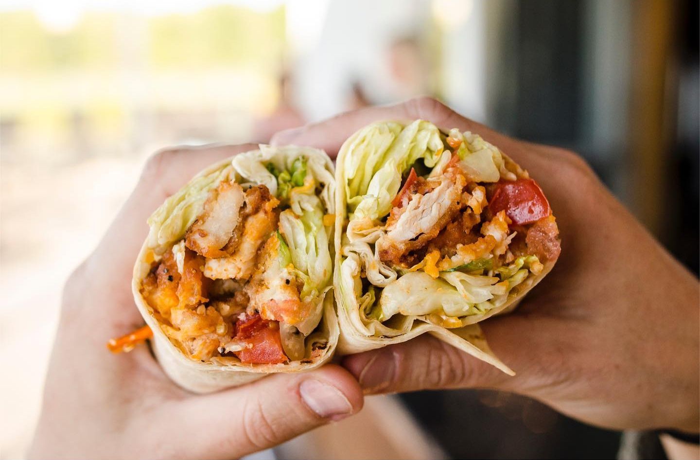 Hands holding a cut wrap, showing chicken, lettuce, tomato, and dressing.