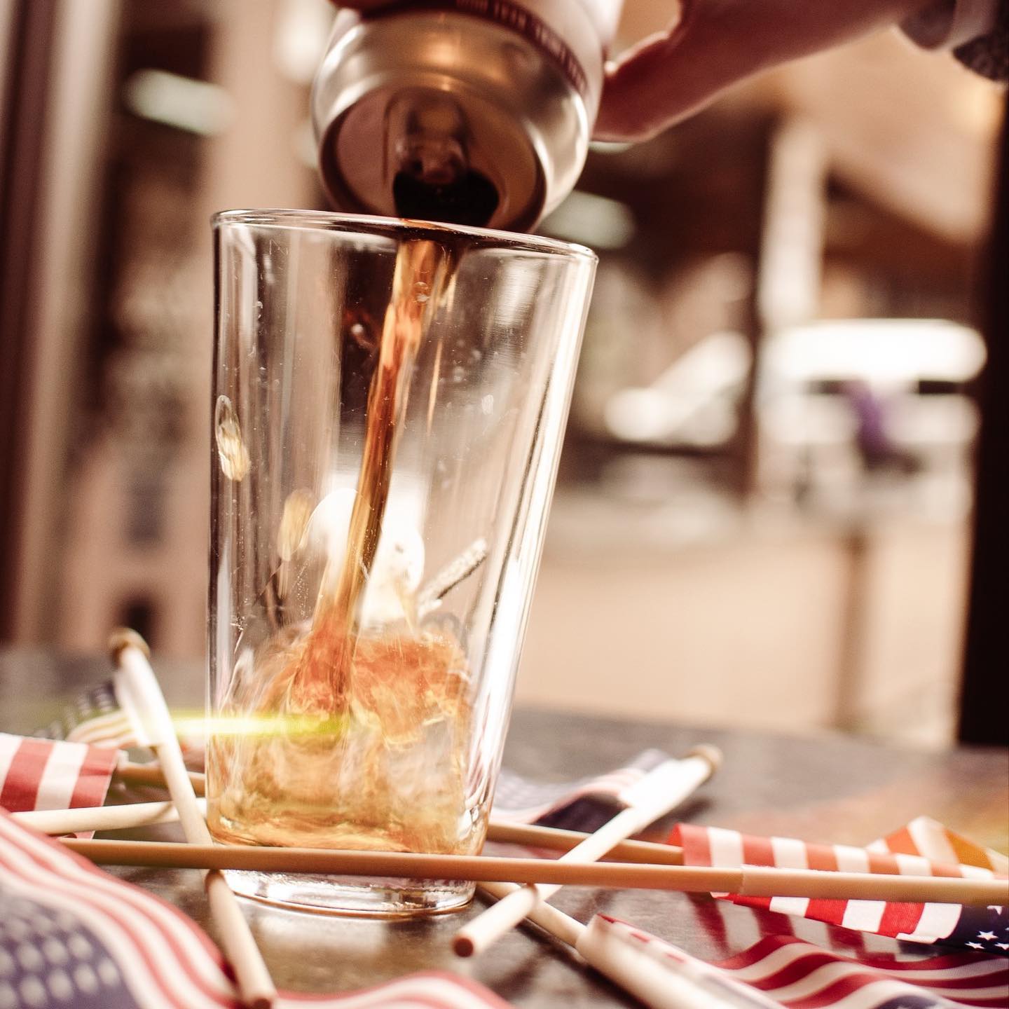 Pouring a drink from a can into a glass with small American flags on a table.