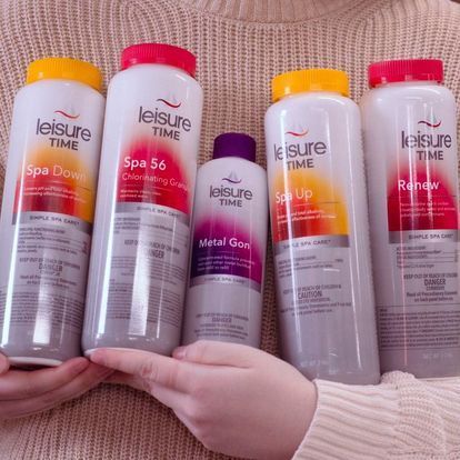 Person holding five spa chemical bottles: Spa Down, Spa 56, Metal Gon, Spa Up, and Renew.