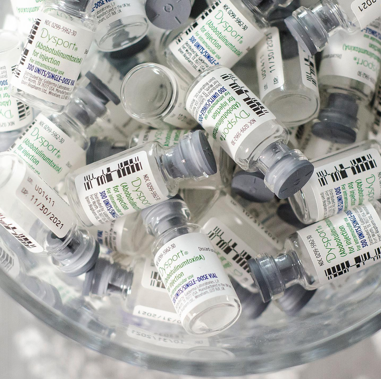 Vials of Dysport medication; glass containers with gray caps and white labels, in a clear bowl.