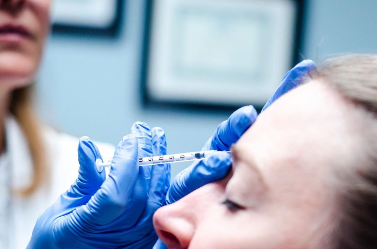 Person receiving an injection in the forehead from a gloved hand in a medical setting.