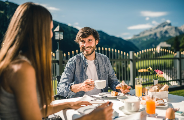 Man and woman enjoying breakfast outdoors with mountain backdrop.