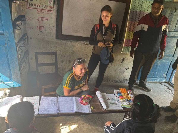 People in a classroom, looking at a desk with books and papers. One woman wears an Australia shirt.