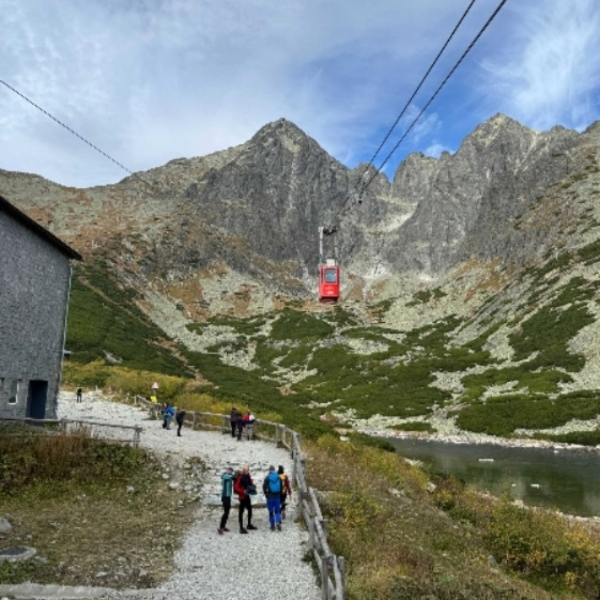 Cable car ascending a mountain in the High Tatras, Slovakia. People walk along a path near a lake.