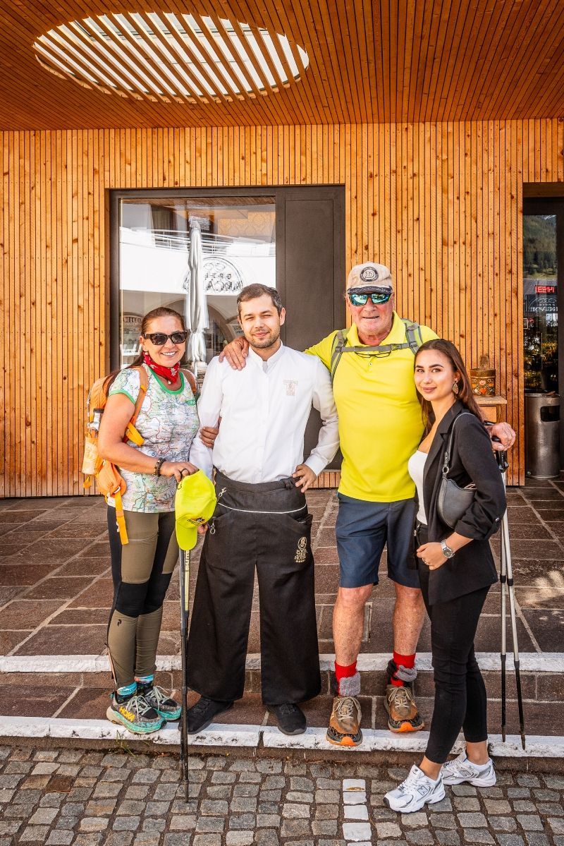 Two women pose by a sign at Passo Giau, Italy. One gives a thumbs up, both smiling. They are hiking.