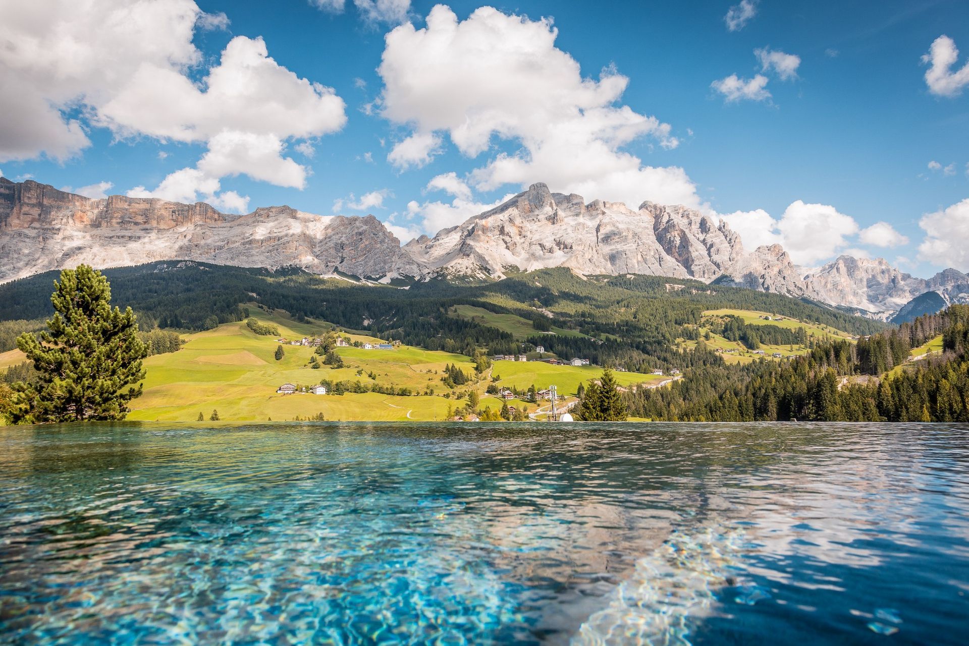Infinity pool overlooking lush green hills and mountains under a blue sky.