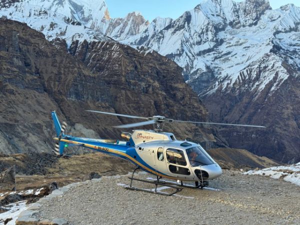 Helicopter on a rocky landing pad, snow-capped mountains in the background, blue and silver color scheme.