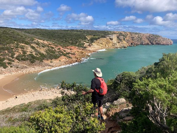 Man with backpack overlooking a turquoise bay, surrounded by cliffs and vegetation.