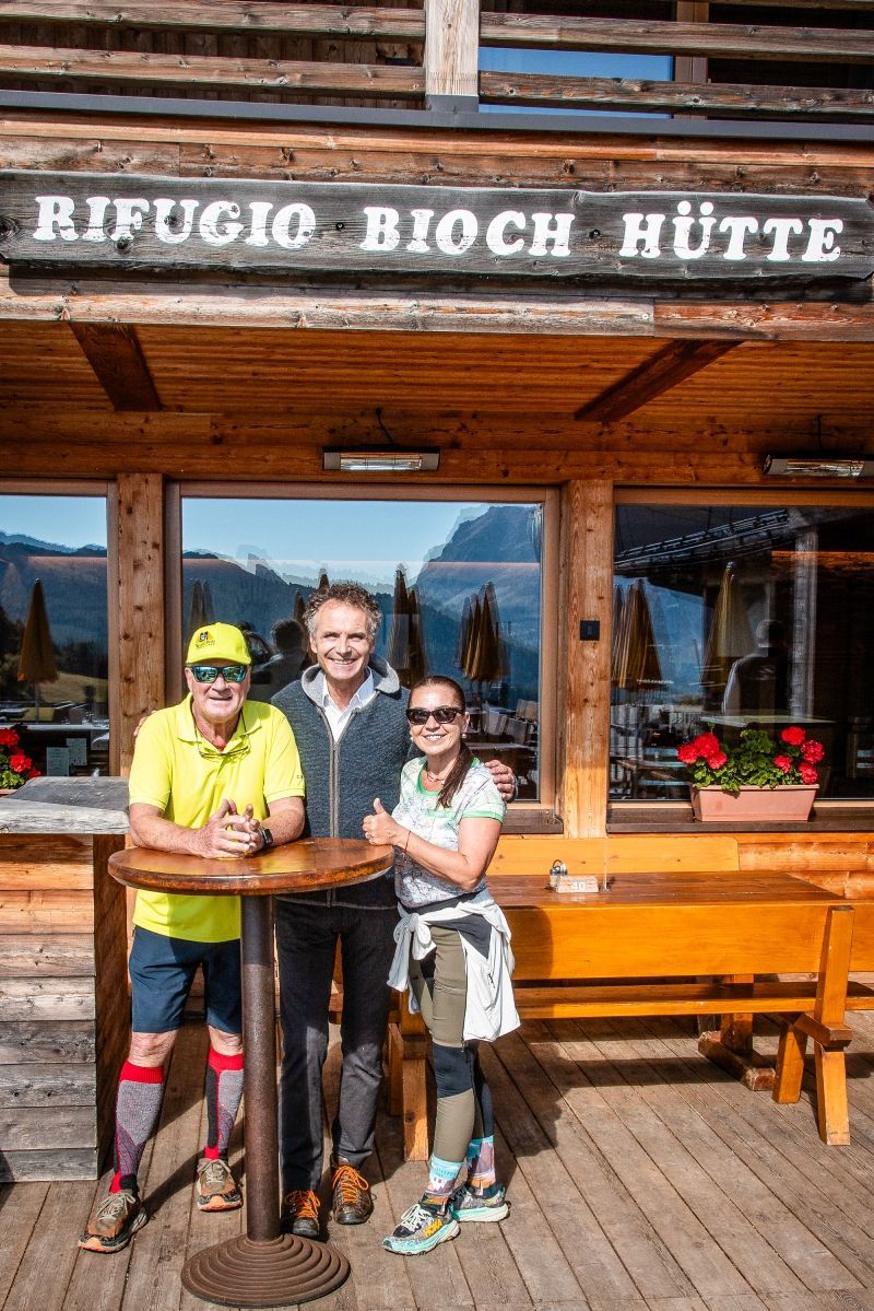 Group of hikers posing on a dirt path in front of a mountain range under a blue sky.