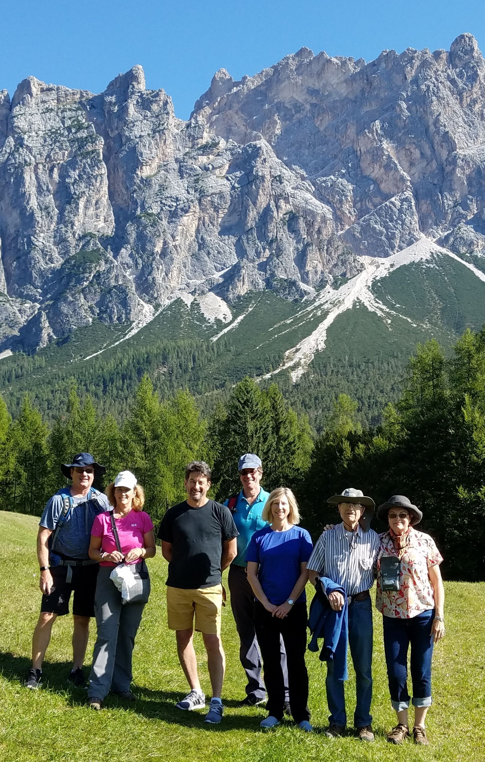 Group of people standing on a grassy area, mountain range in the background, sunny day.