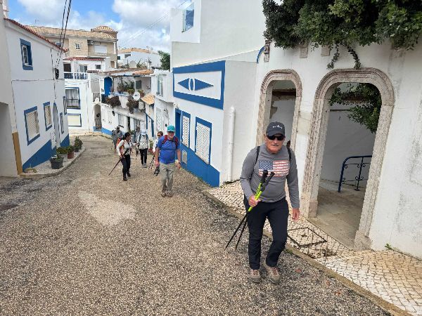 People walking uphill on a cobblestone street lined with white buildings with blue trim.