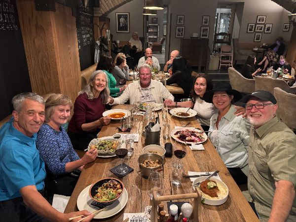 People seated at a wooden table in a restaurant, eating and smiling. Dimly lit with warm tones.