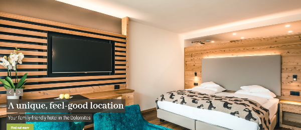 Hotel room with wooden walls, a large TV, and a bed with a patterned blanket.