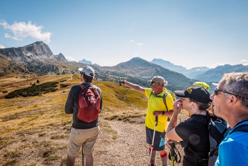 Group hiking in mountains, man pointing. Sunny day.