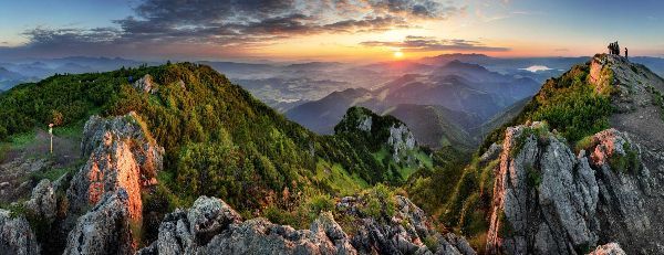 Sunset over lush green mountains with rocky foreground.