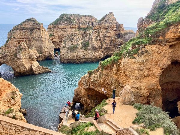 Coastal cliffs and rock formations with turquoise water and people.