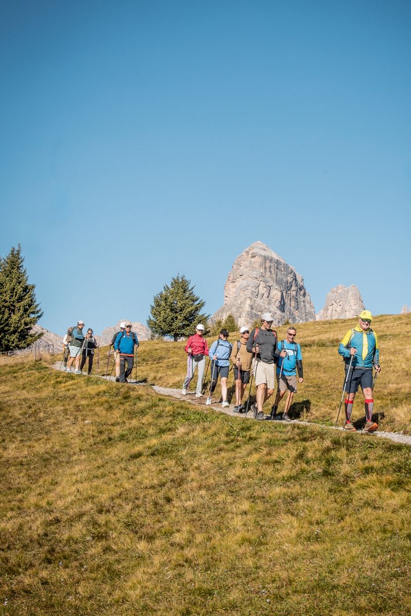 Group of hikers on a trail in a sunny, mountainous landscape with a clear blue sky.