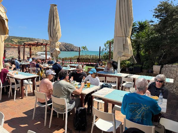 Outdoor cafe with people eating at tables, overlooking a coastal view on a sunny day.