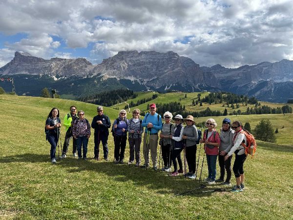 Group of hikers on a grassy hillside, mountains in background. Blue sky with clouds.