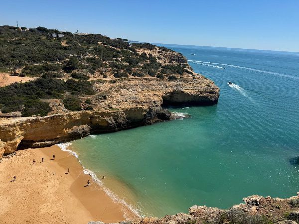 Sandy beach nestled in cliffs, turquoise water, boat on the sea, sunny day.
