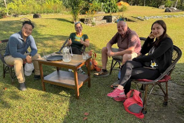 Four people seated outdoors around a table on a grassy lawn.