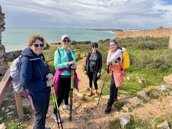 Four people with hiking poles pose on a trail near the ocean.