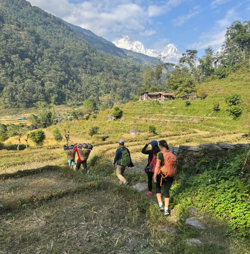 Hikers walk on a path through terraced fields, mountains in the distance.