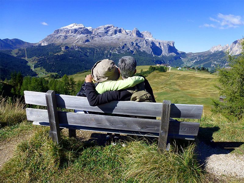Couple on bench, embracing, overlooking mountains and valley on a sunny day.
