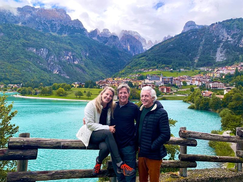 Three people pose by turquoise lake, mountains behind.