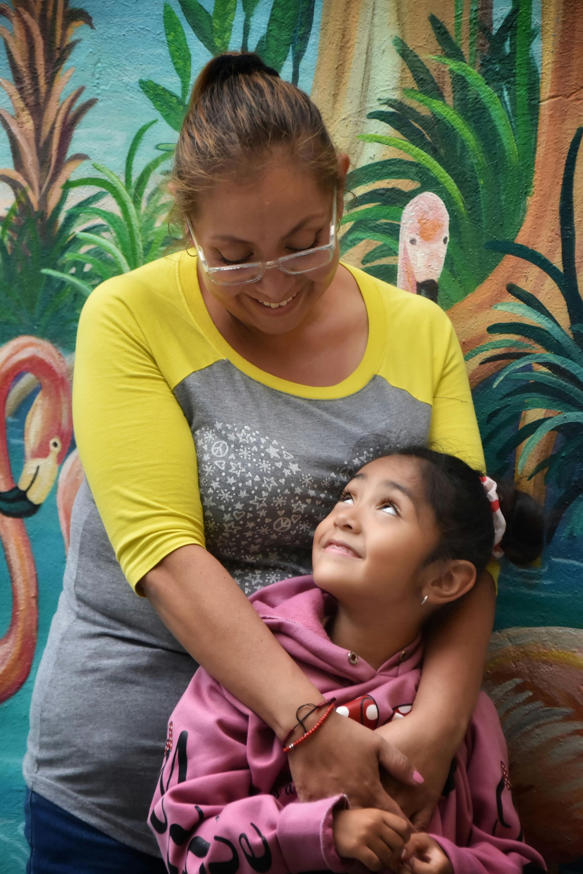 Mujer abrazando a un niño, mirándose cariñosamente frente a un fondo de flamencos pintados.