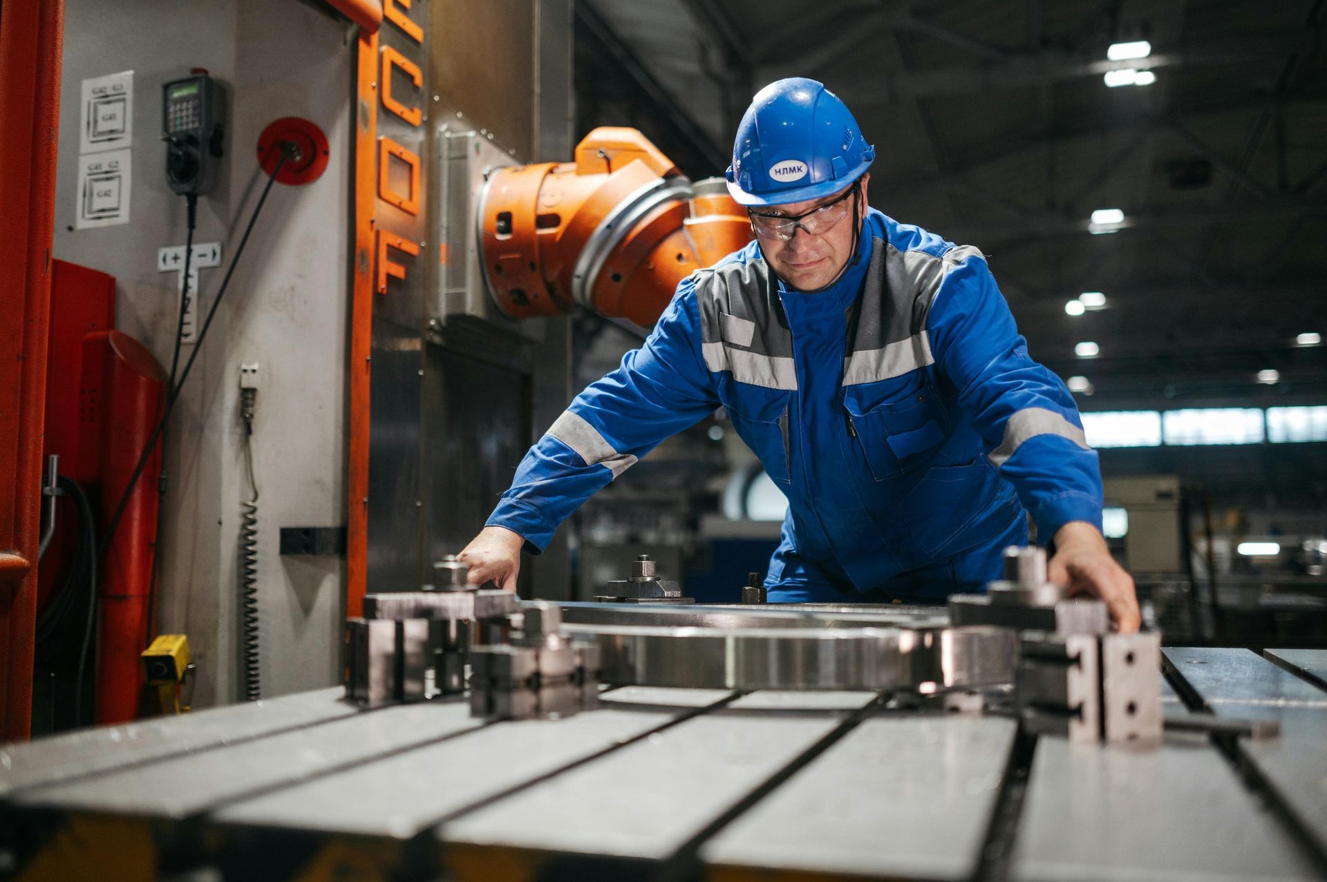 Un hombre con traje de trabajo azul y casco trabaja en una máquina en una fábrica.