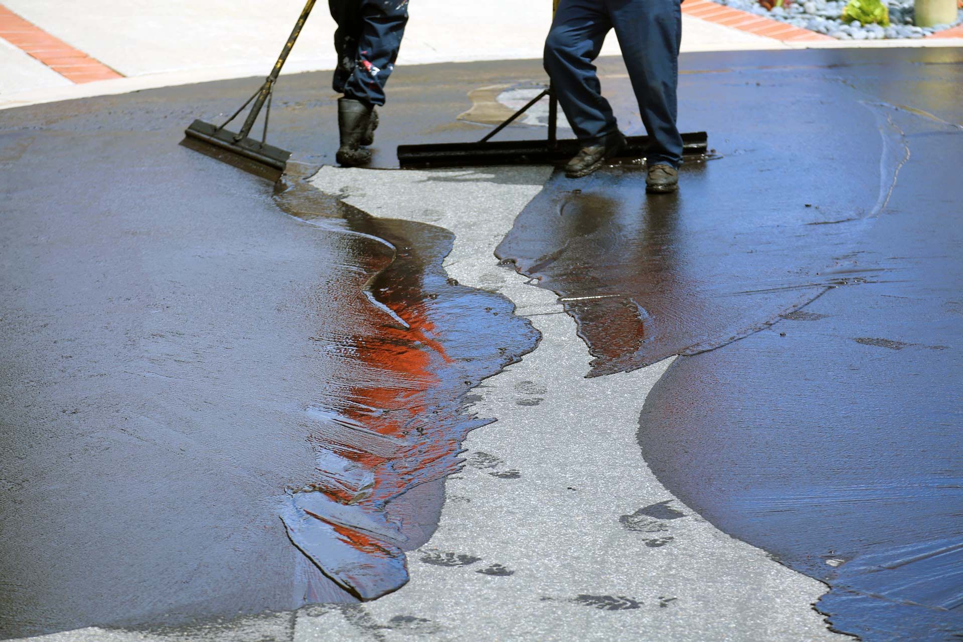 A man is using a broom to spread asphalt on the ground.