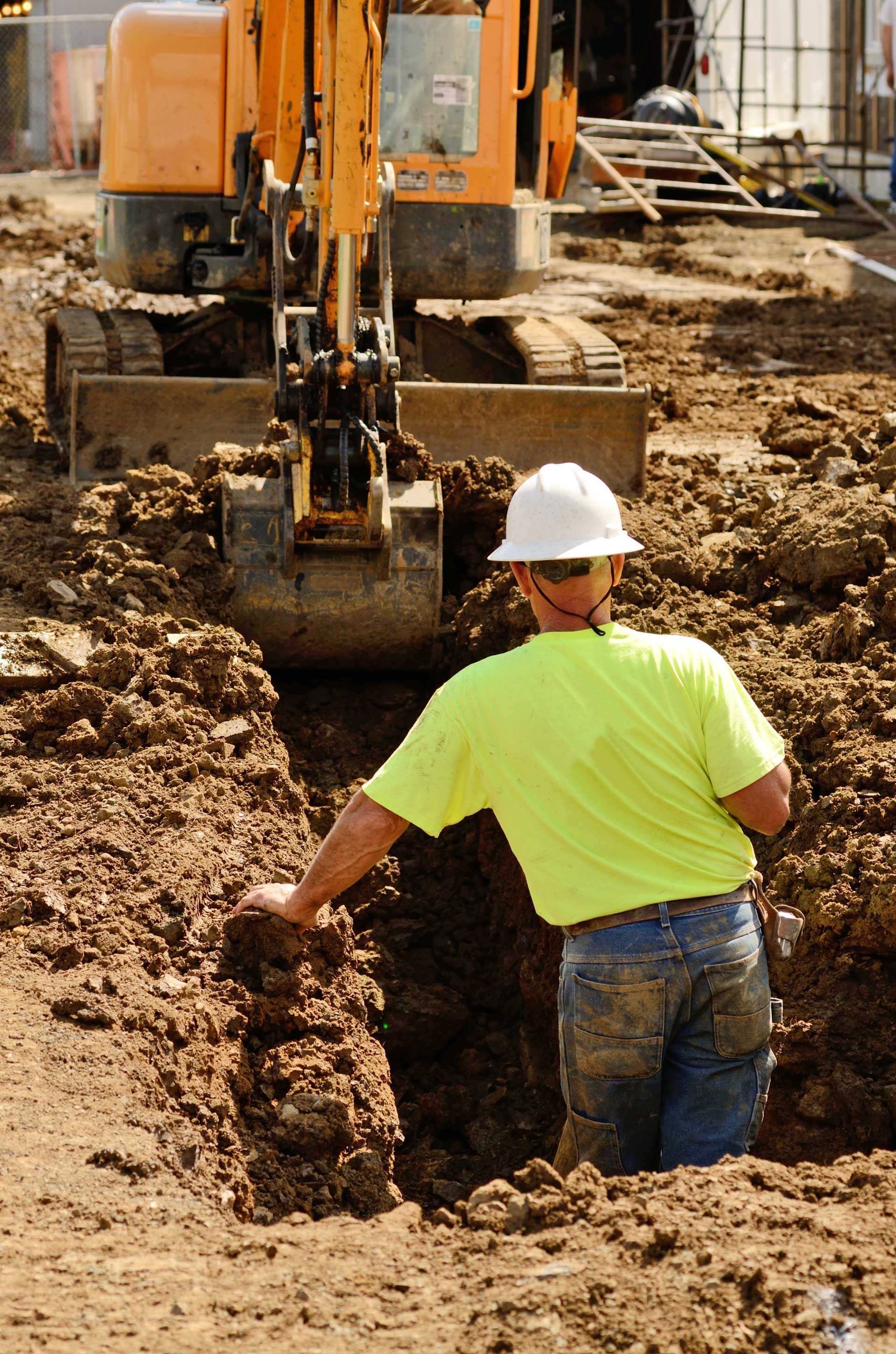 A man wearing a hard hat and a yellow shirt is digging in the dirt