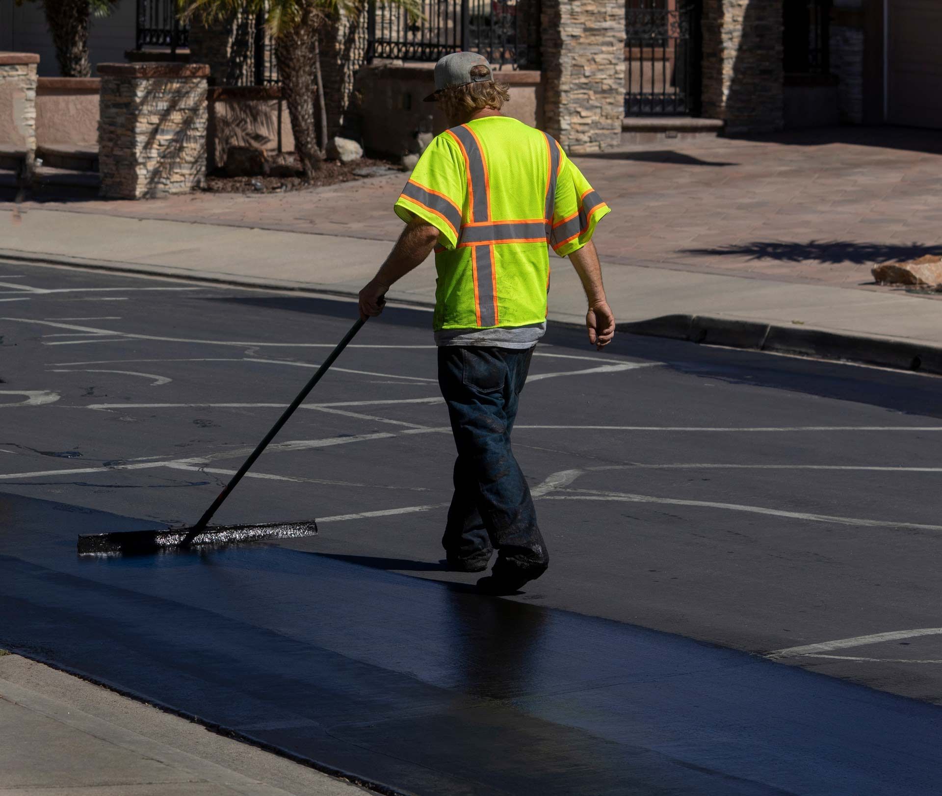 A man in a yellow vest is spreading asphalt on the ground