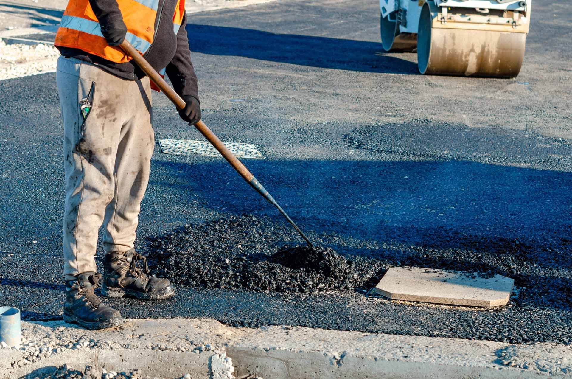 A man is spreading asphalt on a road with a shovel