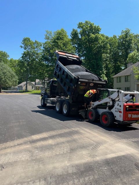 A dump truck is being towed by a bobcat skid steer.