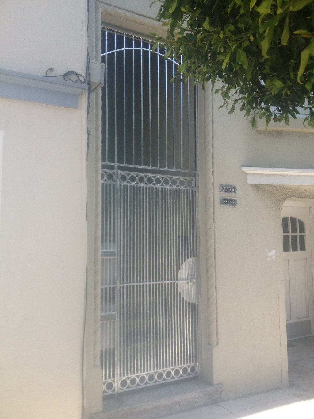 A white building with a metal gate and a tree in front of it