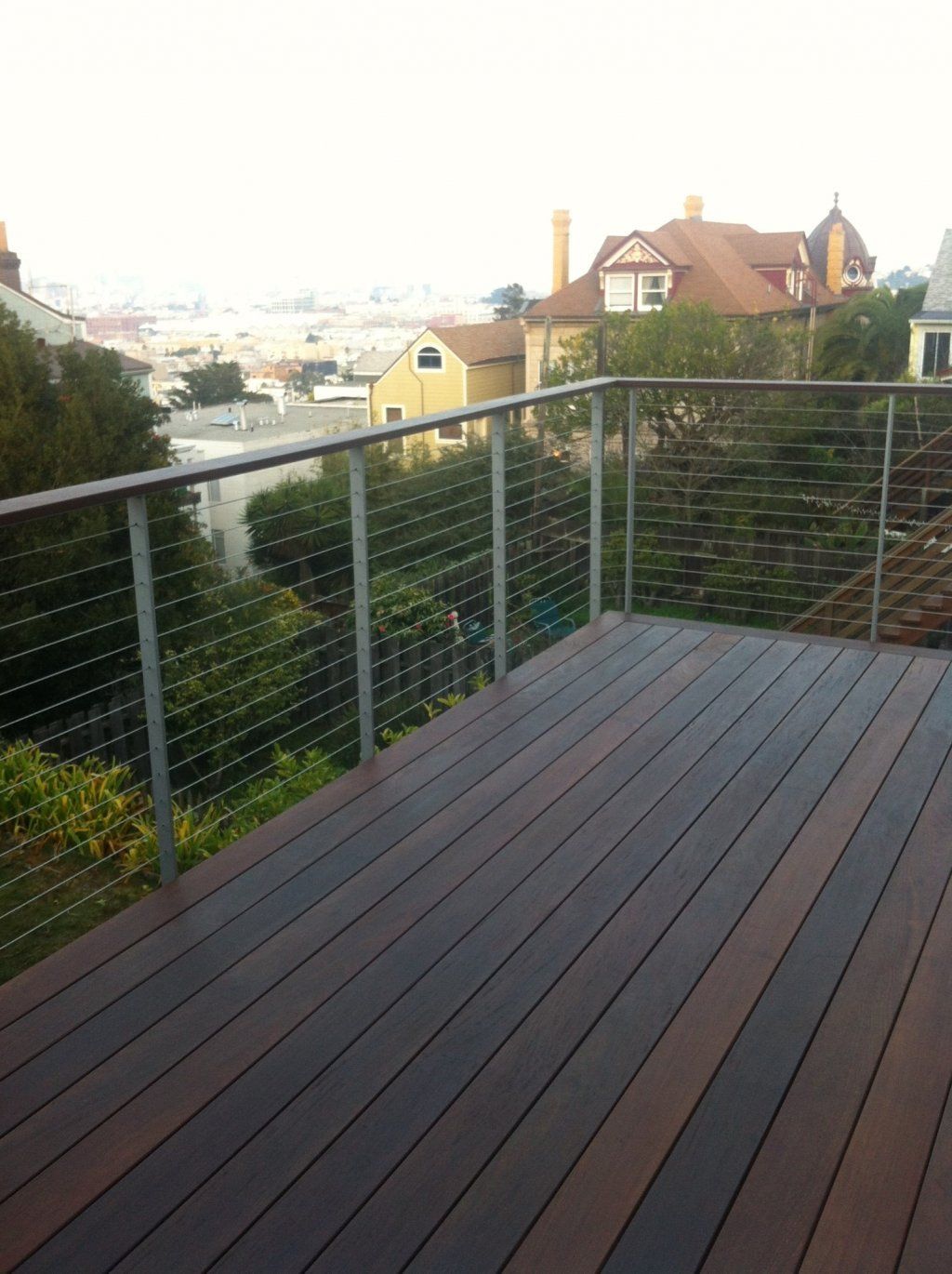 A wooden deck with a stainless steel railing overlooking a city