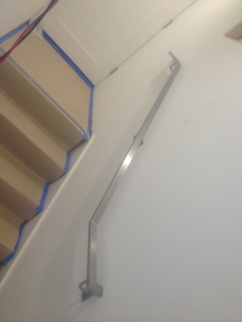 A staircase with blue tape on the steps and a metal railing on the wall.