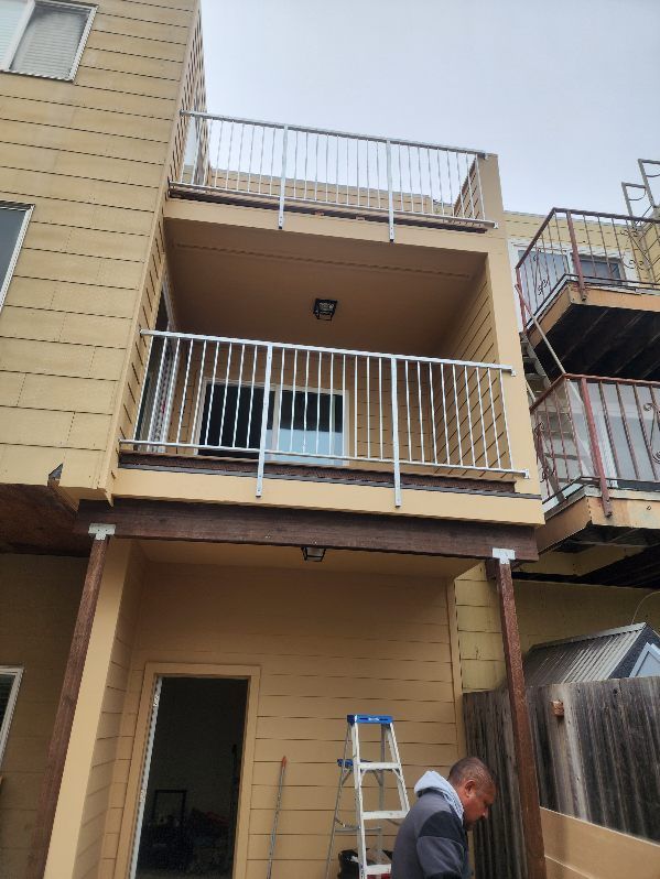 A man is standing on a ladder in front of a building with a balcony.