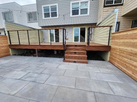 A wooden deck with stairs leading up to it is in the backyard of a house.