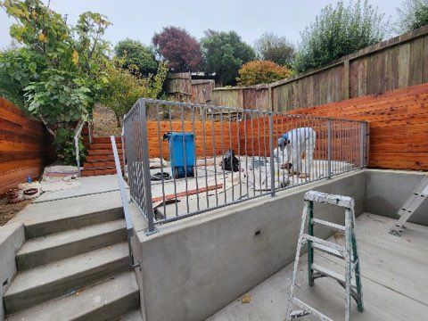 A man is working on a metal railing in a backyard.