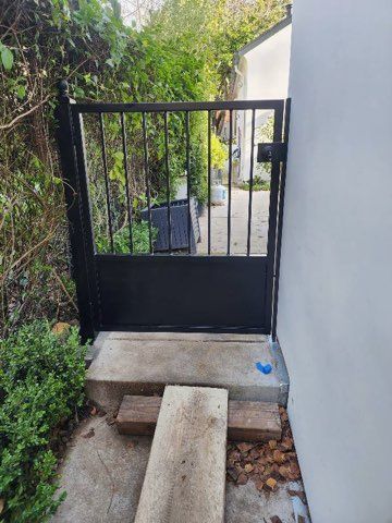A black gate is sitting on the side of a building next to a stone bench.
