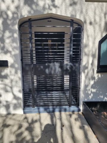A window with a metal fence around it and a shadow of trees on the wall.