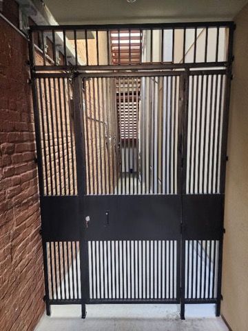 A black gate is sitting in a hallway next to a brick wall.