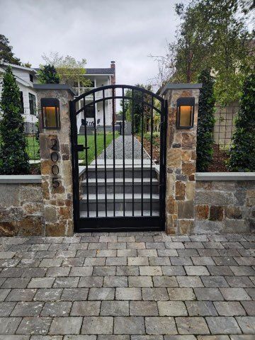 A wrought iron gate is surrounded by stone pillars and steps leading to a house.
