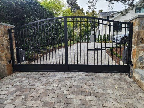 A black gate is sitting on a brick driveway in front of a house.