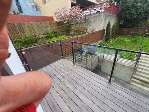A person is sitting on a wooden deck with a glass railing.